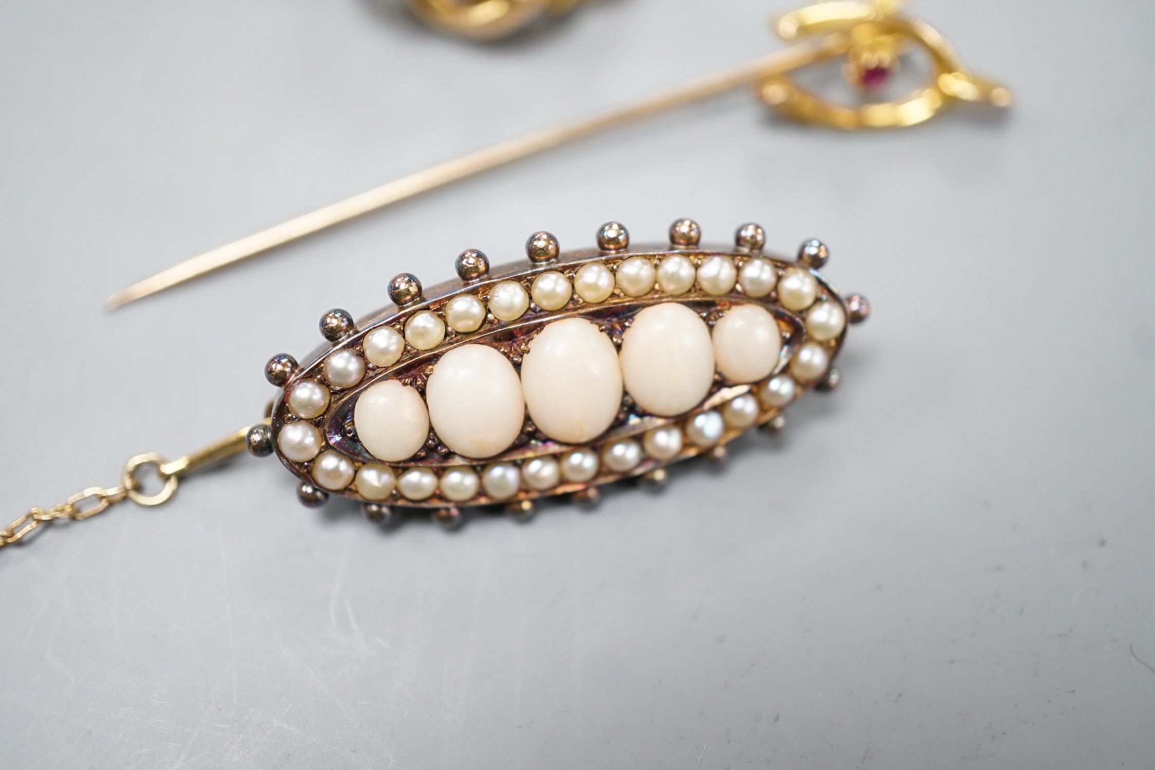 An Edwardian yellow metal, turquoise and split pearl set openwork brooch, 22mm, a similar coral and split pearl set ovoid brooch and a 15ct and gem set wish bone stick pin, gross weight 14.3 grams.